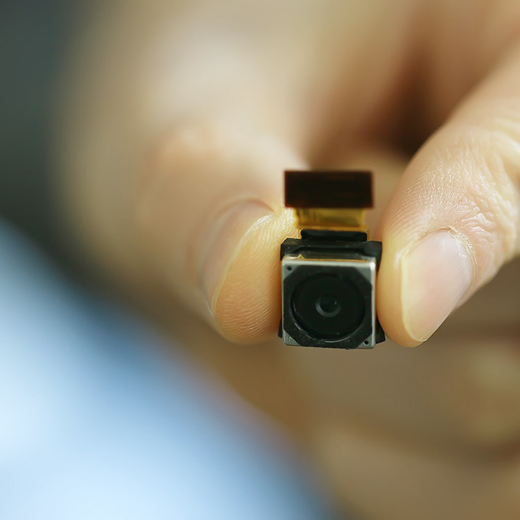 Person holding a miniaturised surveillance camera between their fingers